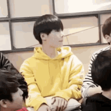 a boy in a yellow hoodie is sitting in a room with other people .