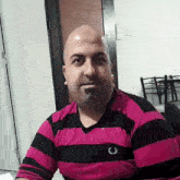 a bald man wearing a pink and black striped shirt with the letter c on the chest