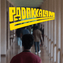 a man is walking down a hallway with the word padakkamam on the wall behind him