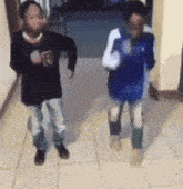 two young boys are dancing in a hallway with one wearing a black shirt with the letter b on it