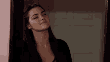 a woman with long dark hair is standing in front of a door with her eyes closed .