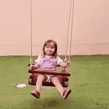 a little girl is sitting on a wooden swing on the grass .