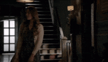 a woman in a dress and cardigan stands in front of stairs