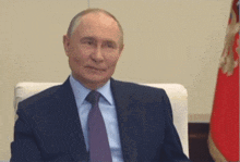 a man in a suit and tie sits in front of a red flag