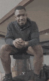 a man in a black hoodie is sitting on a chair with his legs crossed