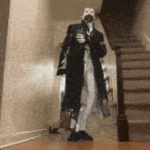 a man in a black coat is standing in a hallway with stairs