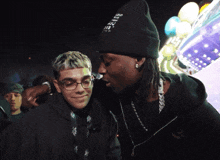a man wearing a beanie that says " i love you " talks to another man