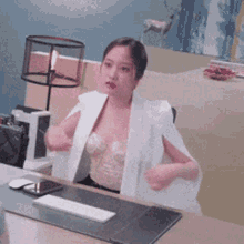 a woman is sitting at a desk wearing a white jacket