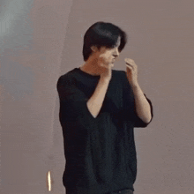 a young man in a black shirt is standing in front of a wall and making a funny face .