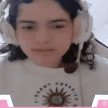 a woman wearing headphones and a white shirt with a sun on it looks at the camera