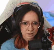 a woman wearing glasses and headphones is sitting in front of a microphone and making a funny face .
