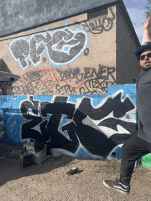 a man wearing sunglasses stands in front of a wall with graffiti on it that says pee