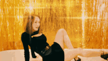 a woman in a black dress is laying on the floor in front of a gold curtain
