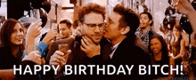 a man is kissing another man on the cheek at a birthday party while holding a glass of champagne .
