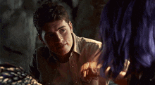 a man and a woman are looking at each other in a dark room . the man has purple hair .