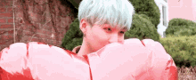 a young man with blue hair is holding a pink heart shaped balloon in front of his face .
