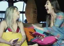two women are sitting on a couch laughing and one is holding a book