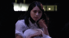 a woman in a white shirt is standing in the dark holding a piece of paper .