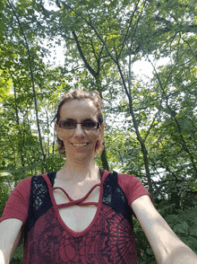 a woman wearing glasses and a red top smiles in front of trees