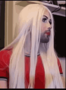 a man with long blonde hair and red lipstick is wearing a red shirt