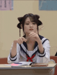 a girl in a sailor suit is sitting at a desk in a classroom holding scissors .