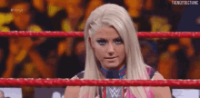 a woman is standing in a wrestling ring holding a microphone and looking at the camera .