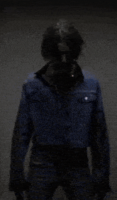 a man in a blue denim jacket is standing in a dark room with his arms outstretched .