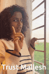 a woman with curly hair is standing in front of a window with the words trust mallesh below her