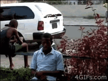 a man is sitting on a bench in front of a white suv with the website 4gifs.com at the bottom of the screen