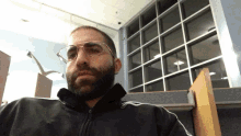 a man with glasses and a beard wears a black jacket