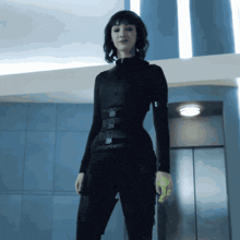 a woman in a black suit is standing in front of a blue wall