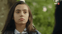 a girl in a school uniform looks at the camera with a trt 1 logo in the corner