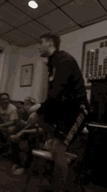 a man in a black shirt and grey shorts stands in a room with other people