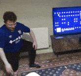 a man wearing a blue shirt that says trusty tour is kneeling in front of a television