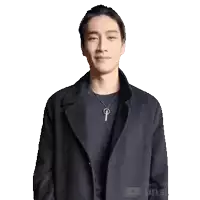 a man wearing a black coat and a necklace is clapping his hands