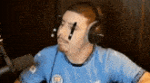a man wearing headphones and a blue shirt is sitting in front of a microphone .