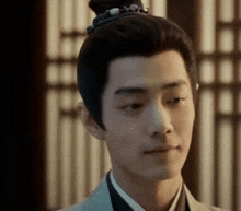a young man with a bun on his head is looking at the camera .