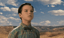 a young boy wearing a bow tie and a plaid shirt looks up at the sky