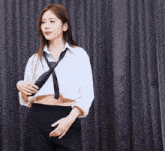 a woman in a white shirt and black tie is standing in front of a curtain