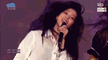 a woman in a white shirt is singing into a microphone on a stage .