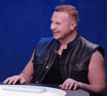 a man wearing a black leather vest is laughing with his mouth open