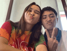 a man and a woman are posing for a picture and the woman is wearing a tie dye shirt with the letter l on it