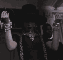a woman wearing a black hat and bracelets holds her hands up in the air