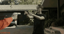 a man is pointing a gun at another man in front of a house with 123witf.me written on the bottom