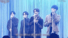 four men are singing into microphones on a stage
