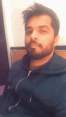 a man with a beard wears a blue hoodie