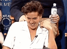 a man is holding a bottle of water and laughing while sitting in a chair .