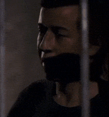 a man in a black shirt is behind bars in a jail cell