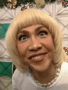 a close up of a woman wearing a blonde wig and a necklace making a funny face .