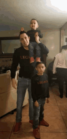 a man is carrying two children on his shoulders while wearing a legacy sweatshirt